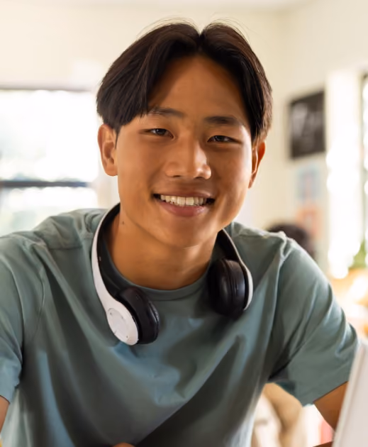 Smiling young man with black headphones around his neck indoors with blurred background.