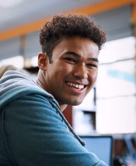 Smiling young man with curly hair wearing a teal hoodie in a bright indoor setting.